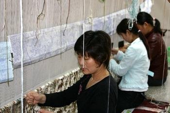 Girls at the loom tying the knots - notice the pattern above their heads